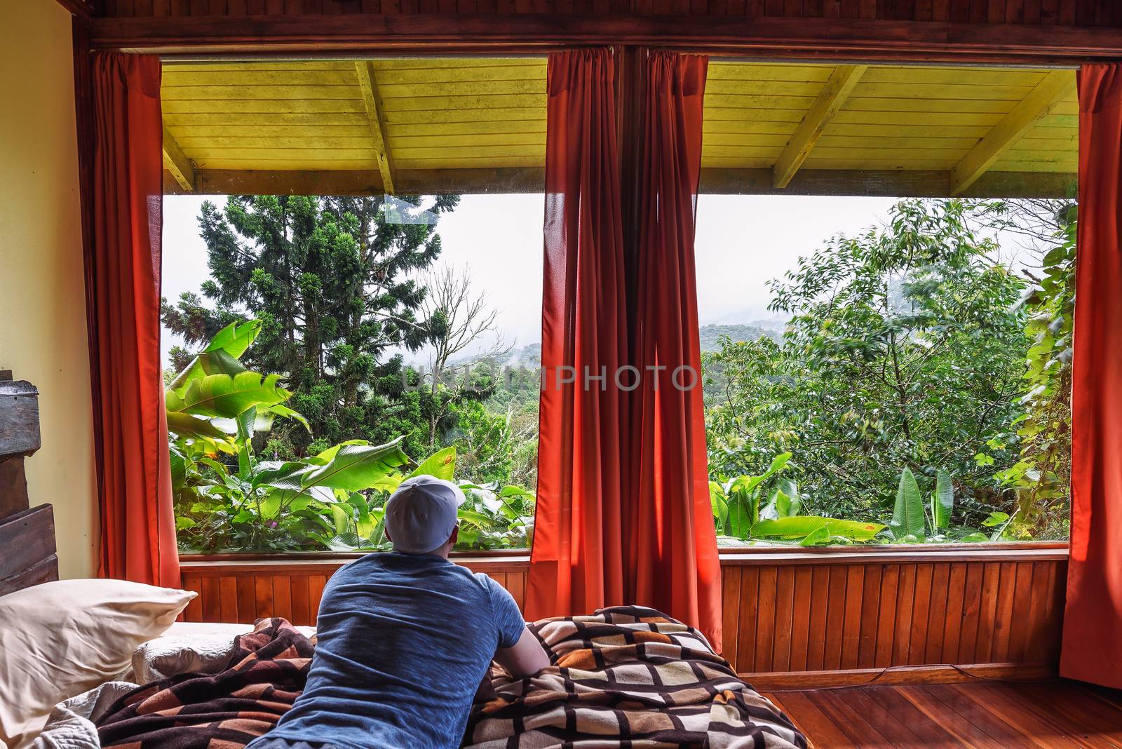 Vara Blanca, Costa Rica - January 13, 2020 : Tourist lying on a bed in Volcan Poas Tiquicia Lodge, a three-star lodge featuring bungalows with volcano views and located close to La Paz Waterfall.