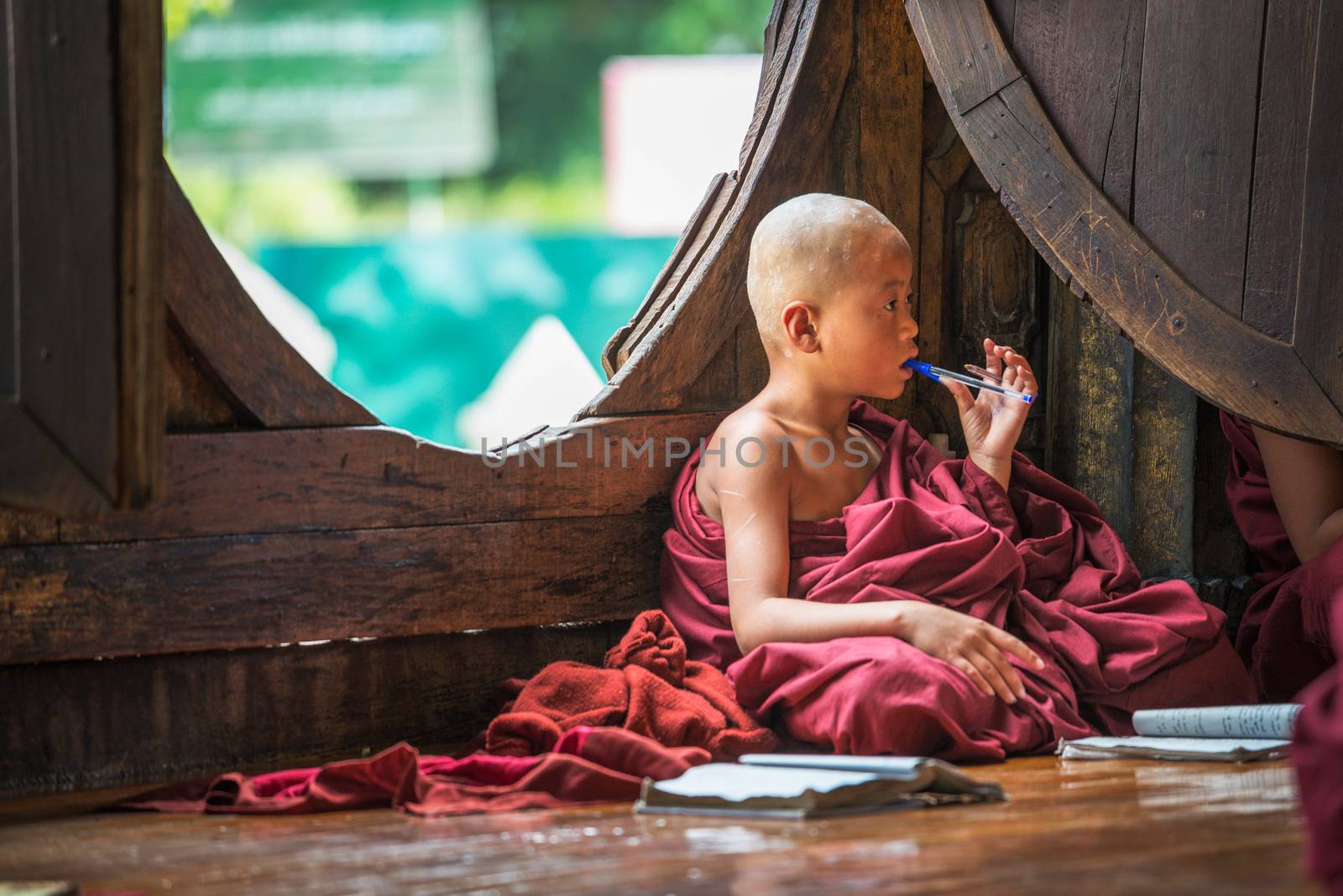 Nyaung Shwe, Myanmar - January 28, 2016 : Southeast Asian child monk learns on the floor of the Shwe Yan Phe Monastery from his school book.