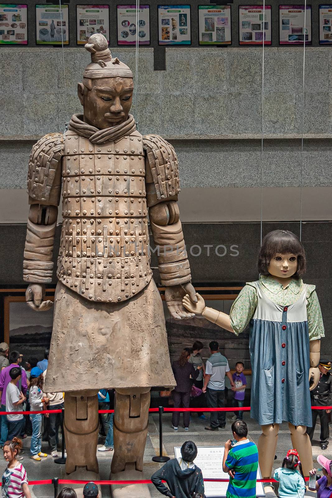 Xian, China - May 1, 2010: Terracotta Army museuml.  Giant light brown sculpture of officer in style holding hand of girl doll about half his size. People around.