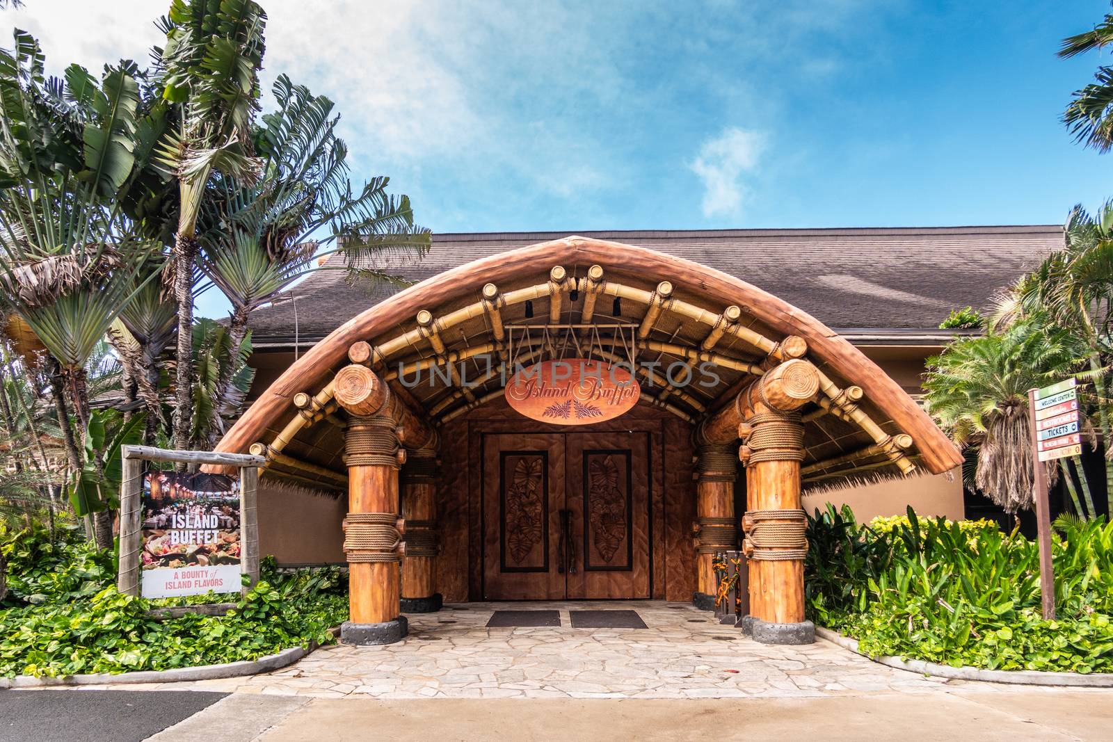 Laie, Oahu, Hawaii, USA. - January 09, 2020: Polynesian Cultural Center. Large wooden entrance to Island Buffet restaurant under blue sky with lots of green vegetation and foliage around.