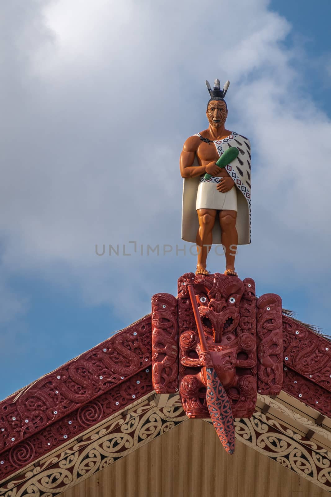Laie, Oahu, Hawaii, USA. - January 09, 2020: Polynesian Cultural Center. Closeup of warrior statue on top of Grand hall with maroon frames of the New Zealand Maori people under blue cloudscape.