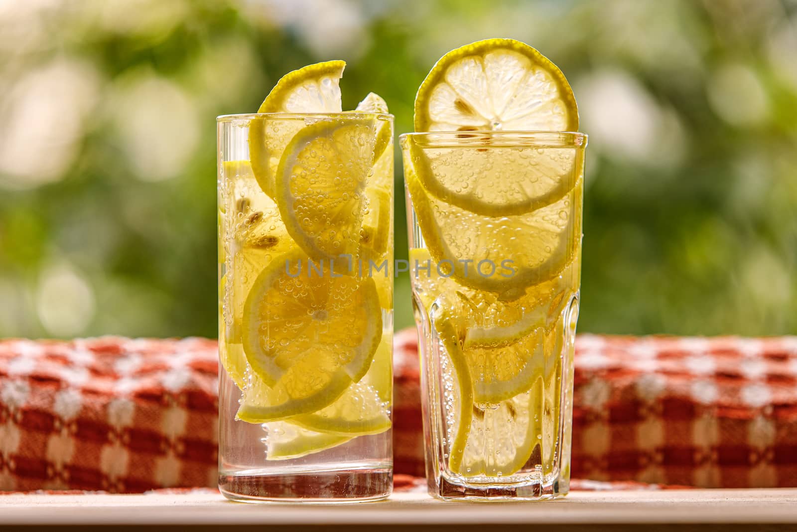 Glasses of lemon water on the sunny garden background