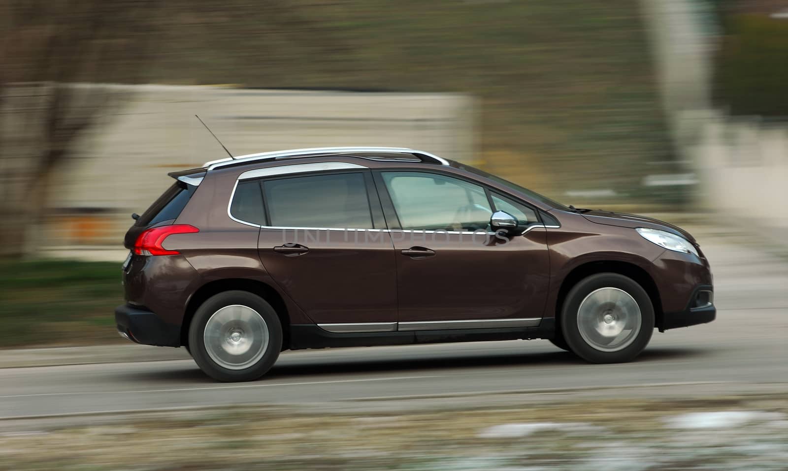 A panning shot of a speeding small brown car