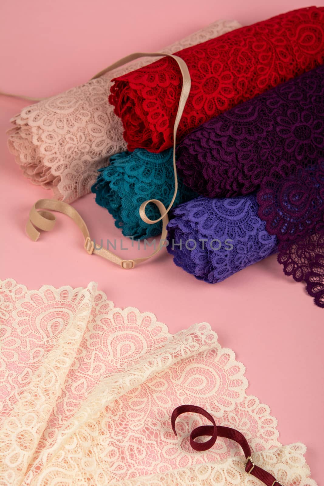 Roll of Delicate color laces for panties and bras on pink background with plastic fittings. Elastic material. Using for Atelier and fabric store.