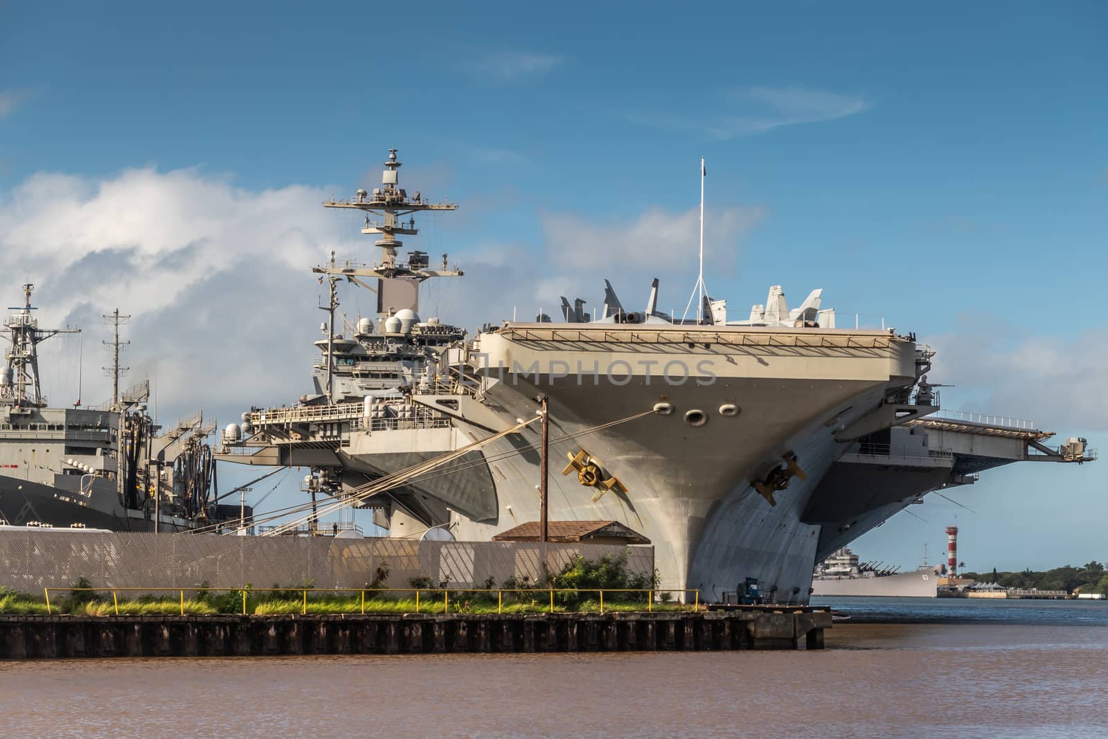 Oahu, Hawaii, USA. - January 10, 2020: Pearl Harbor. Bow of Gray Abraham Lincoln aircraft carrier docked under blue cloudscape on top of brown water.
