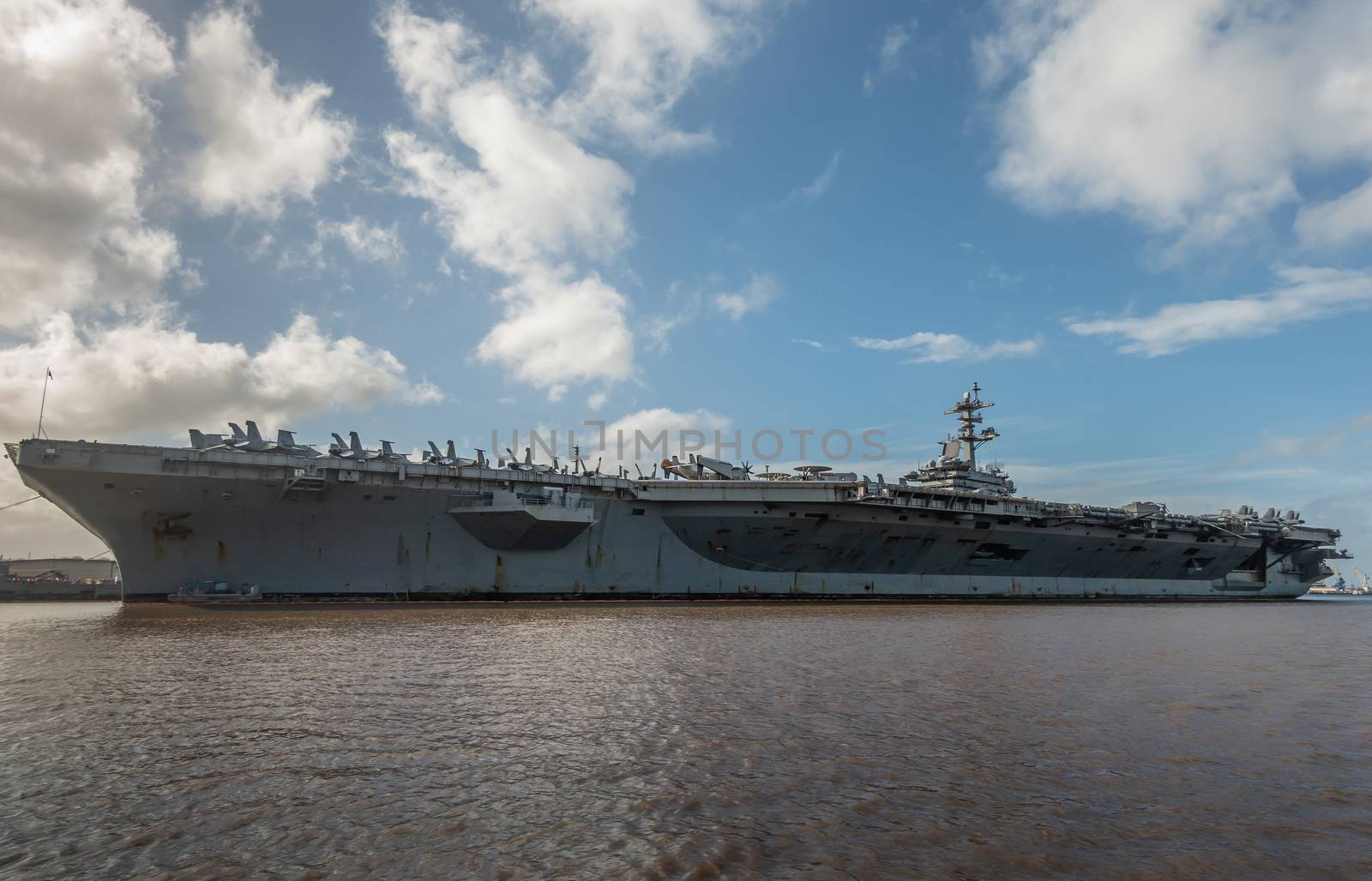 Oahu, Hawaii, USA. - January 10, 2020: Pearl Harbor. Port side of Gray Abraham Lincoln aircraft carrier docked under blue cloudscape on top of brown water.