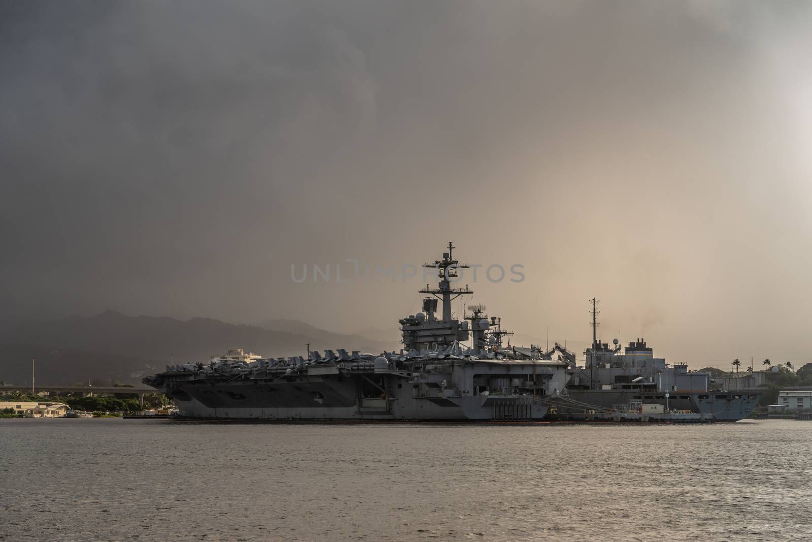 Oahu, Hawaii, USA. - January 10, 2020: Pearl Harbor. Stern of Gray Abraham Lincoln aircraft carrier docked under full rain dark cloudscape on dark gray water.