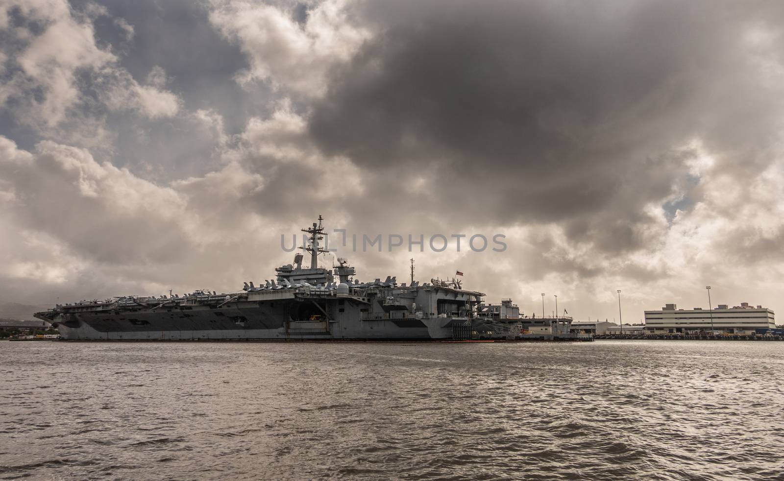 Oahu, Hawaii, USA. - January 10, 2020: Pearl Harbor. Long shot of Gray Abraham Lincoln aircraft carrier docked under full rain dark cloudscape on dark gray water.