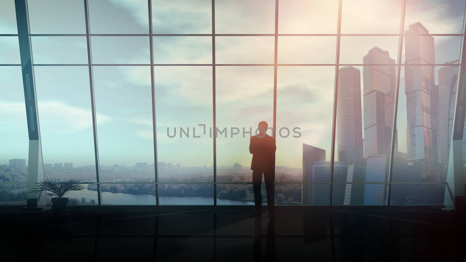 A silhouette of a businessman is looking out of the window of his large office against the backdrop of skyscrapers.