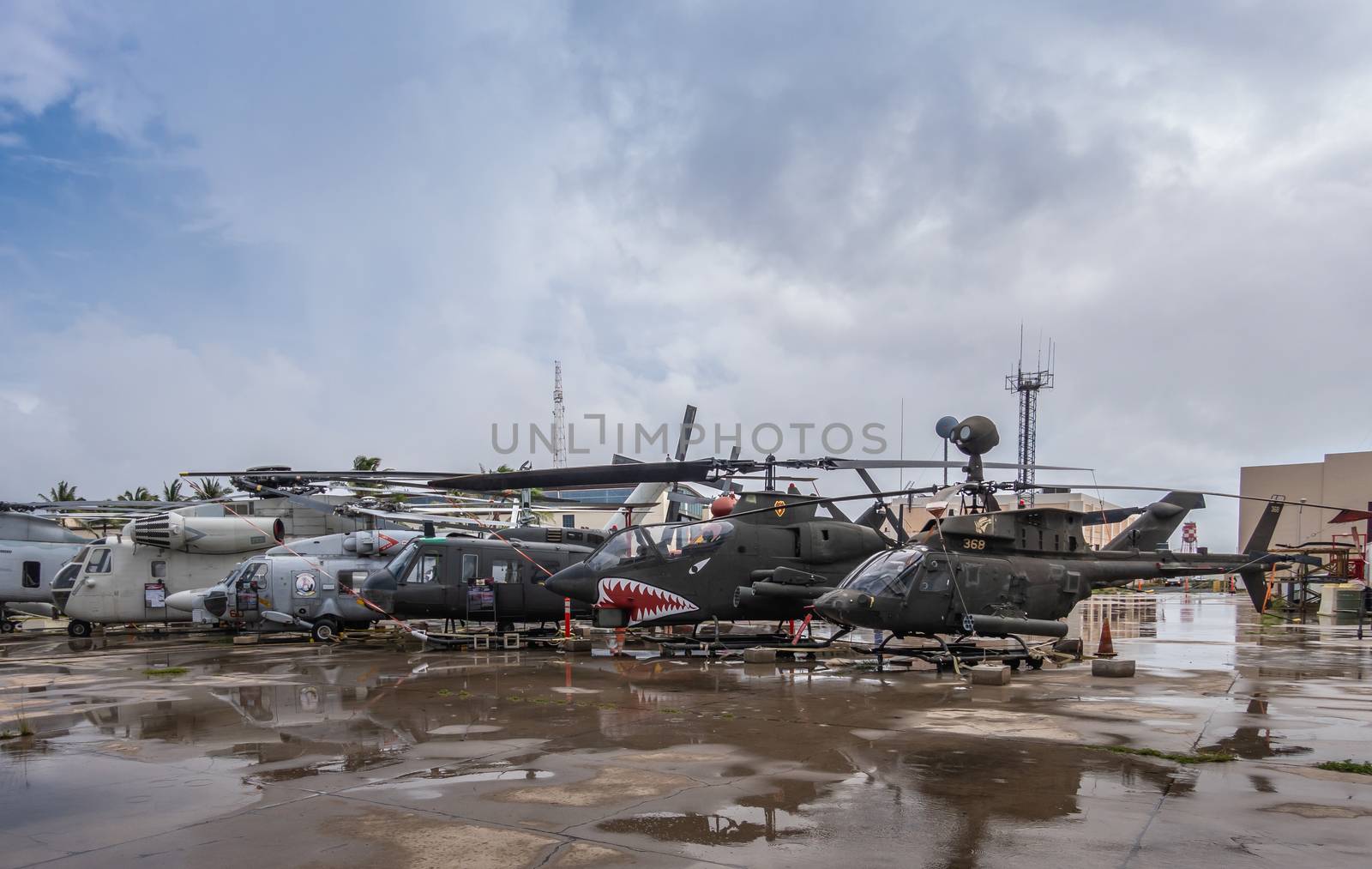 Oahu, Hawaii, USA. - January 10, 2020: Pearl Harbor Aviation Museum. Group of different old helicopters on wet tarmac outside hangar under cloudscape.