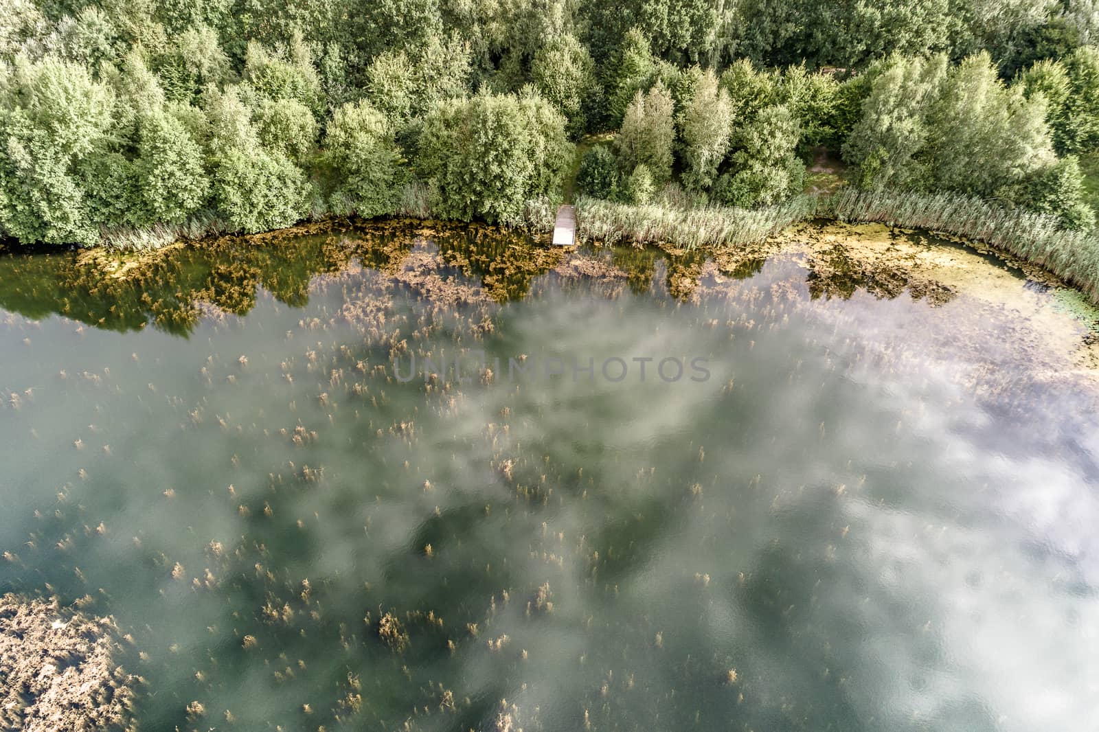 Aerial photo with the drone of the shore of a pond with a footbridge and reflexions of the clouds in the water