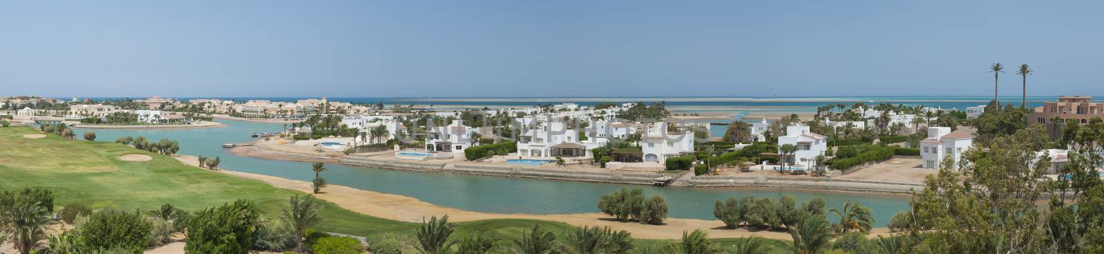 Panoramic aerial view over large coastal lagoon with luxury waterfront villa residences in tropical coastal resort town