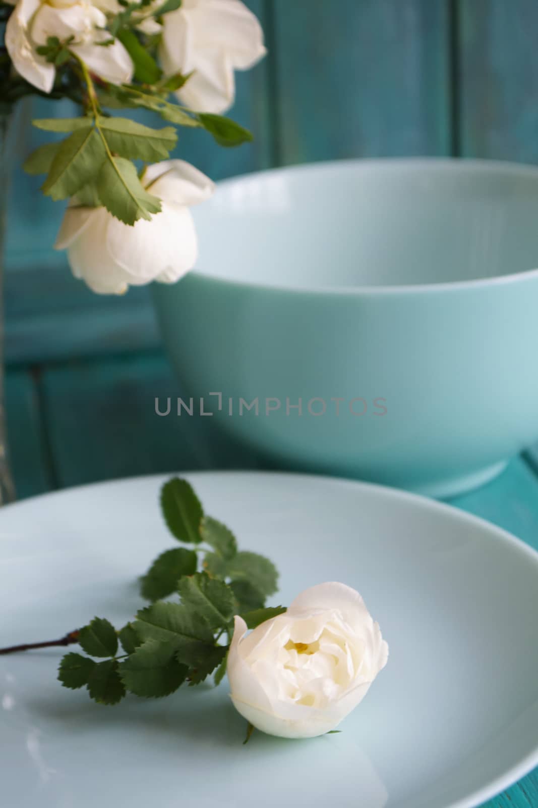 Romantic table setting with bouquet of roses, dishware, on holiday teal table.