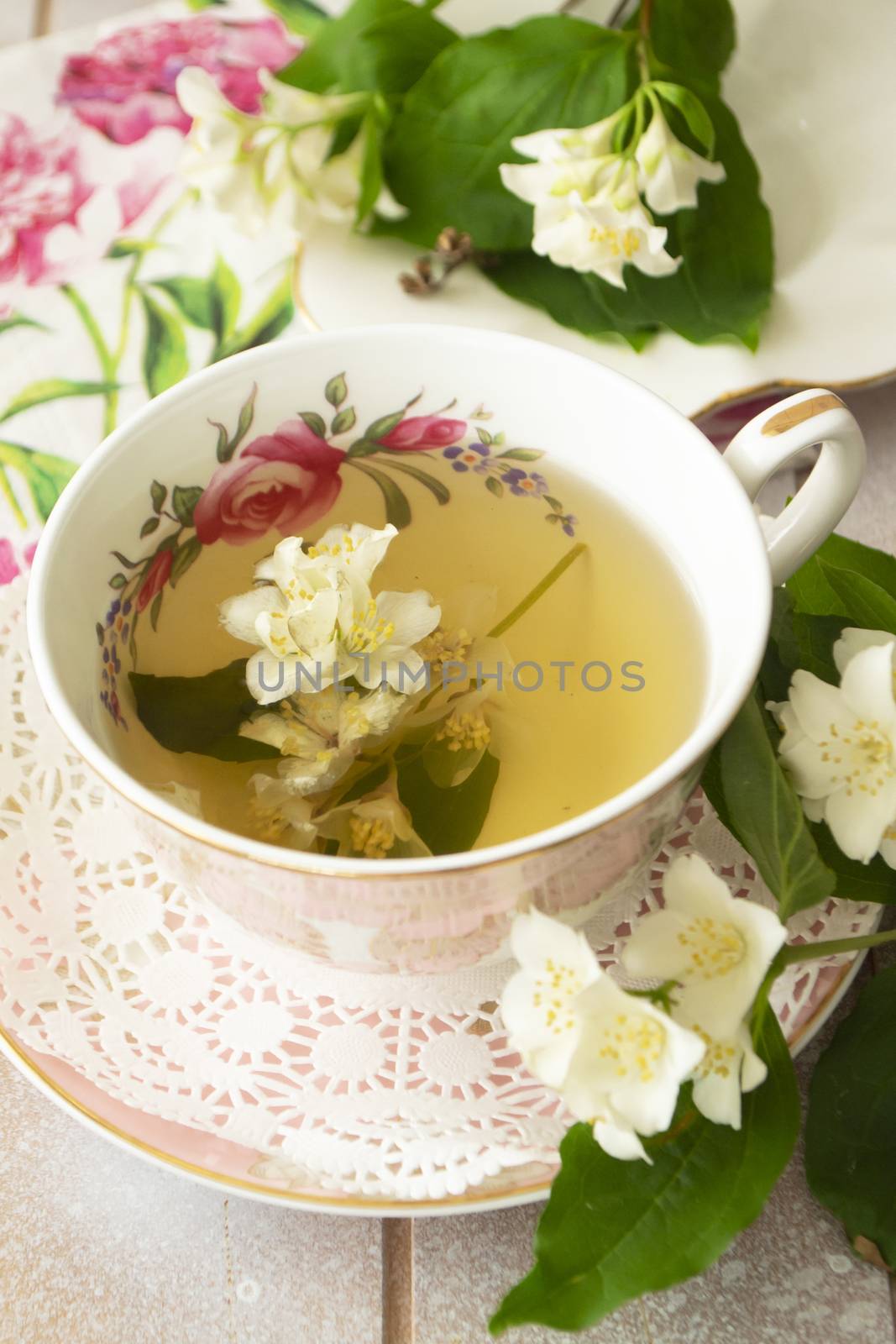 Vintage cup of hot green tea with jasmine flavor and fresh jasmine flowers. Vertical image