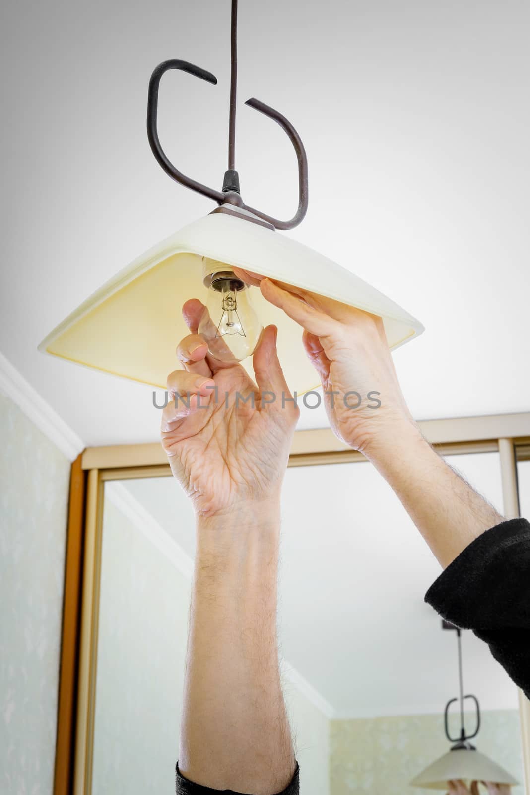 Man installing or changing a bulb, fixing it to the socket at home