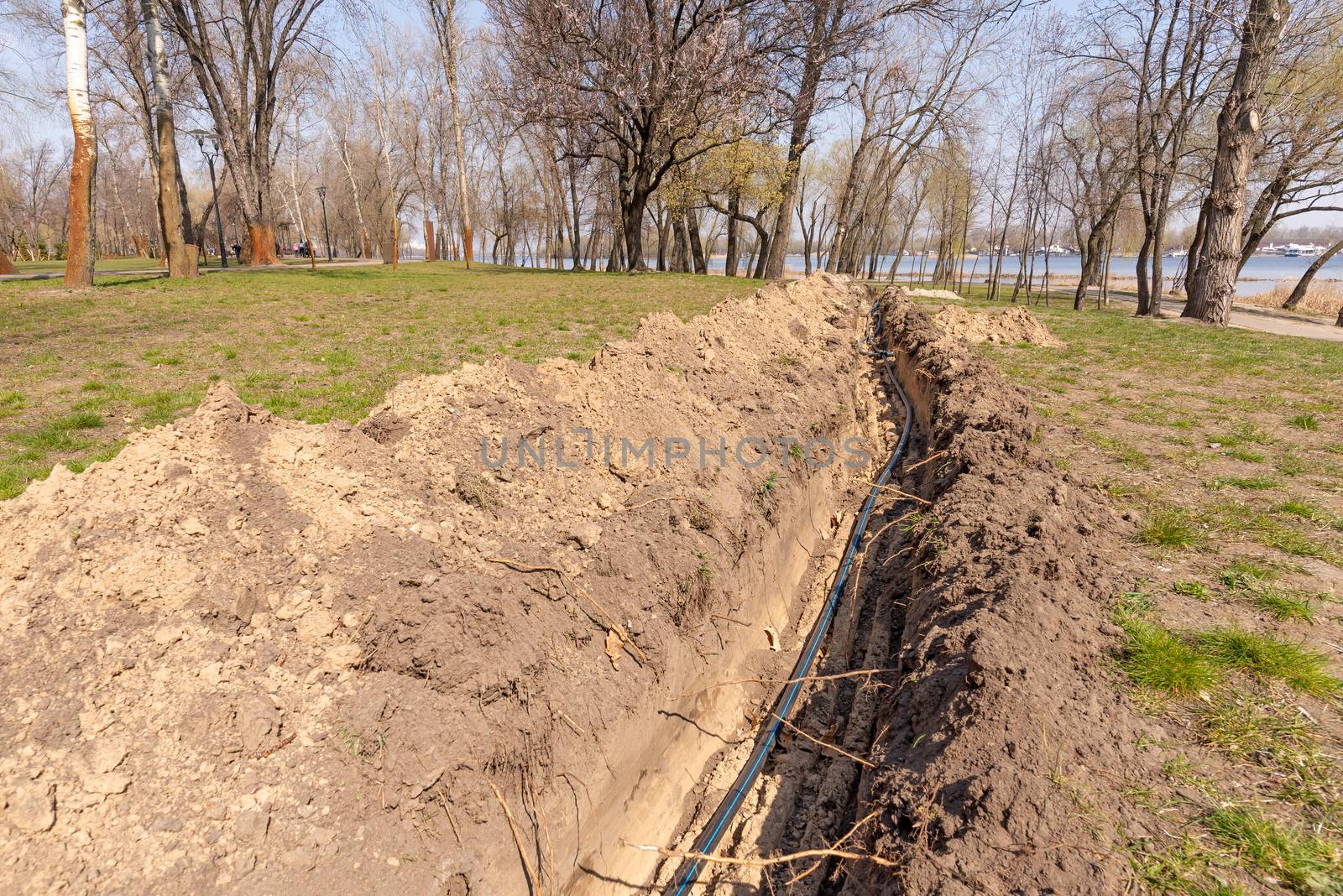Installation of tubes for an irrigation system in the ground under the trees close to the river. Watering system in the Natalka park of Kiev, Ukraine