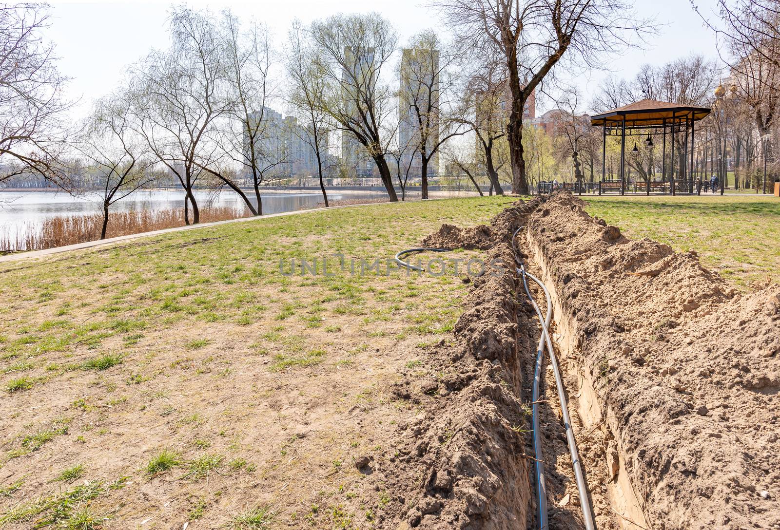 Installation of tubes for an irrigation system in the ground under the trees close to the river. Watering system in the Natalka park of Kiev, Ukraine