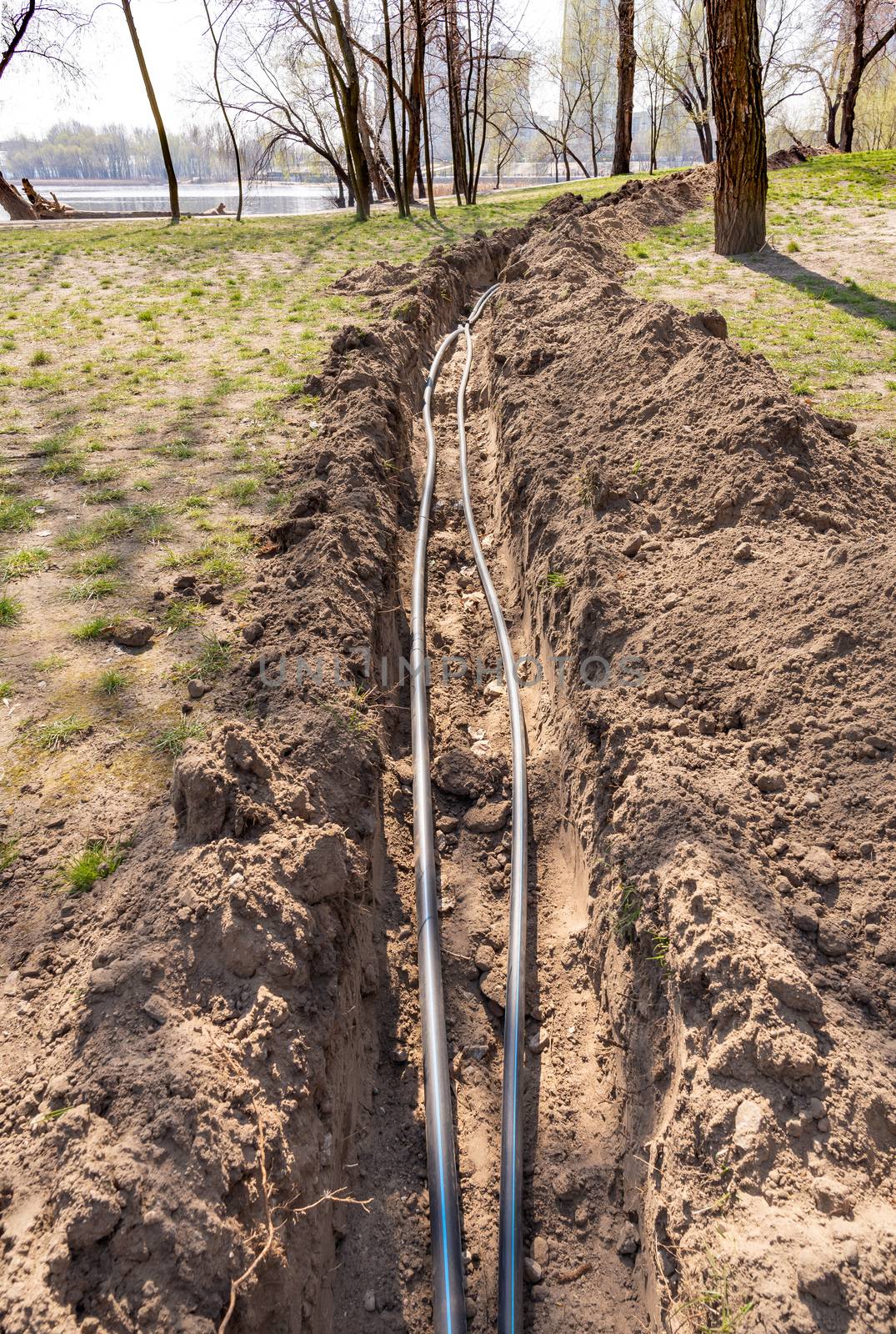 Installation of tubes for an irrigation system in the ground under the trees close to the river. Watering system in the Natalka park of Kiev, Ukraine