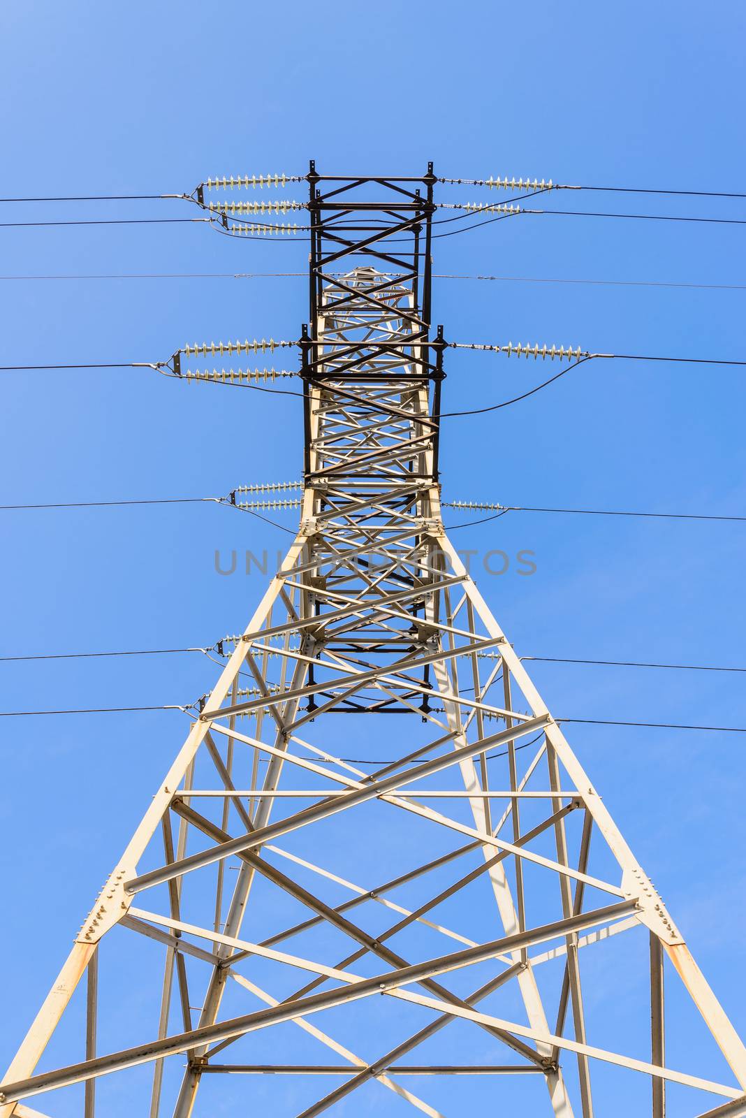 Detail of an electricity pylon against blue sky: high voltage electric cables seen from below