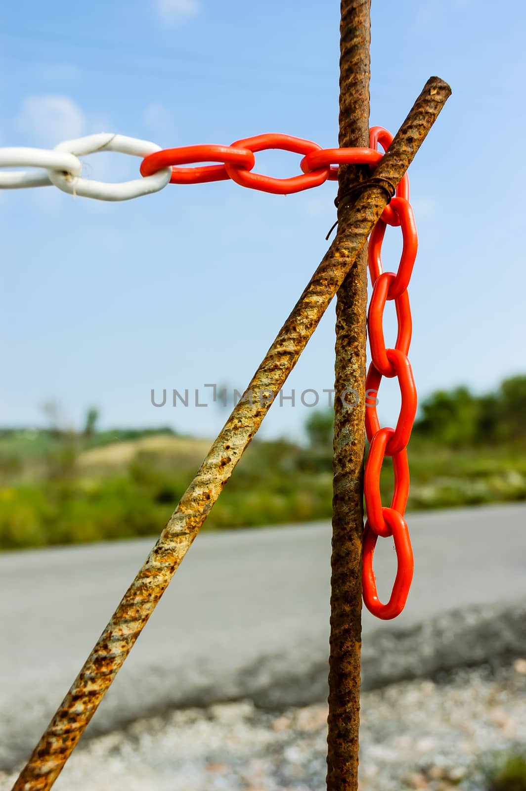 Red and white plastic chain with big links to close the entrance of a site close to the road in the country