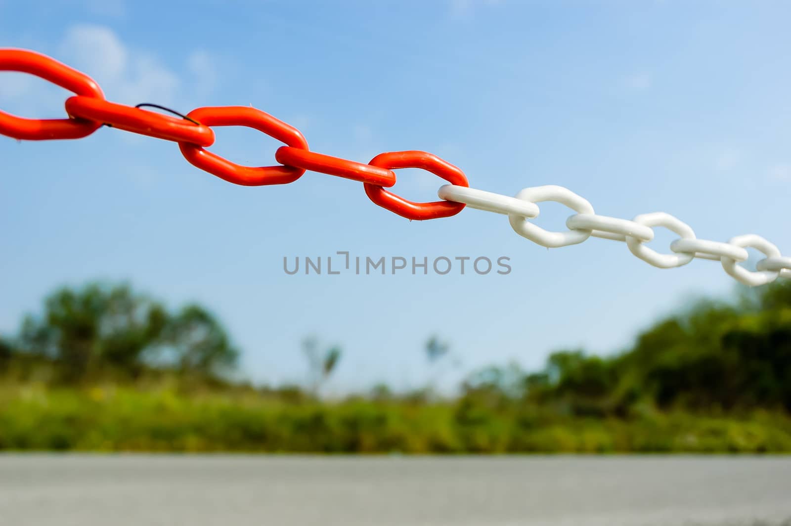 Red and white plastic chain with big links to close the entrance of a site close to the road in the country