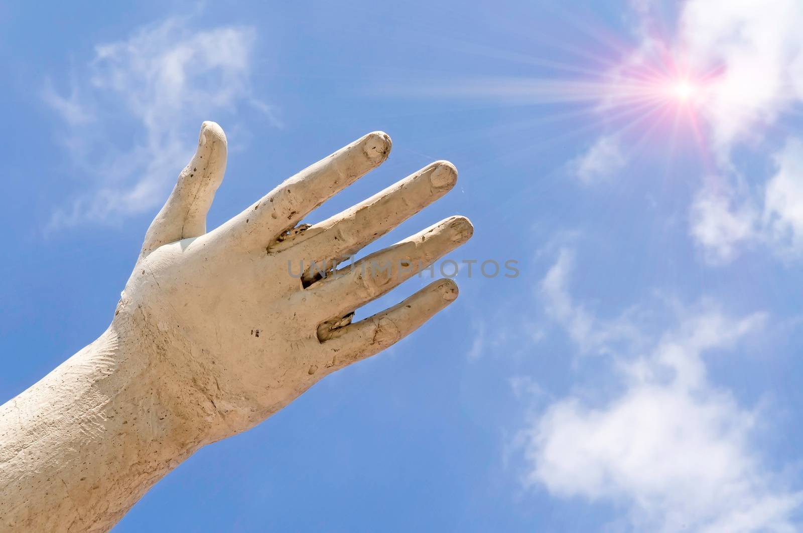 A statue hand showing the sun in the cloudy blue sky, as idea of freedom