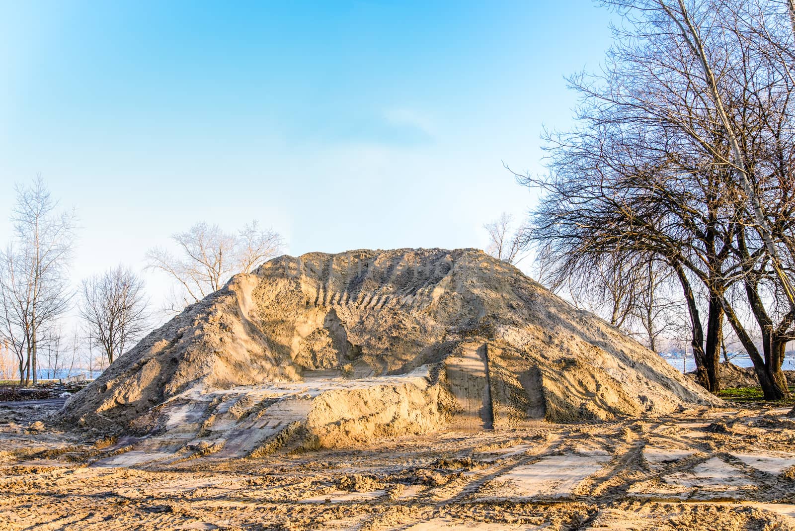 A huge sand heap during construction in the park at sunrise, close to the river