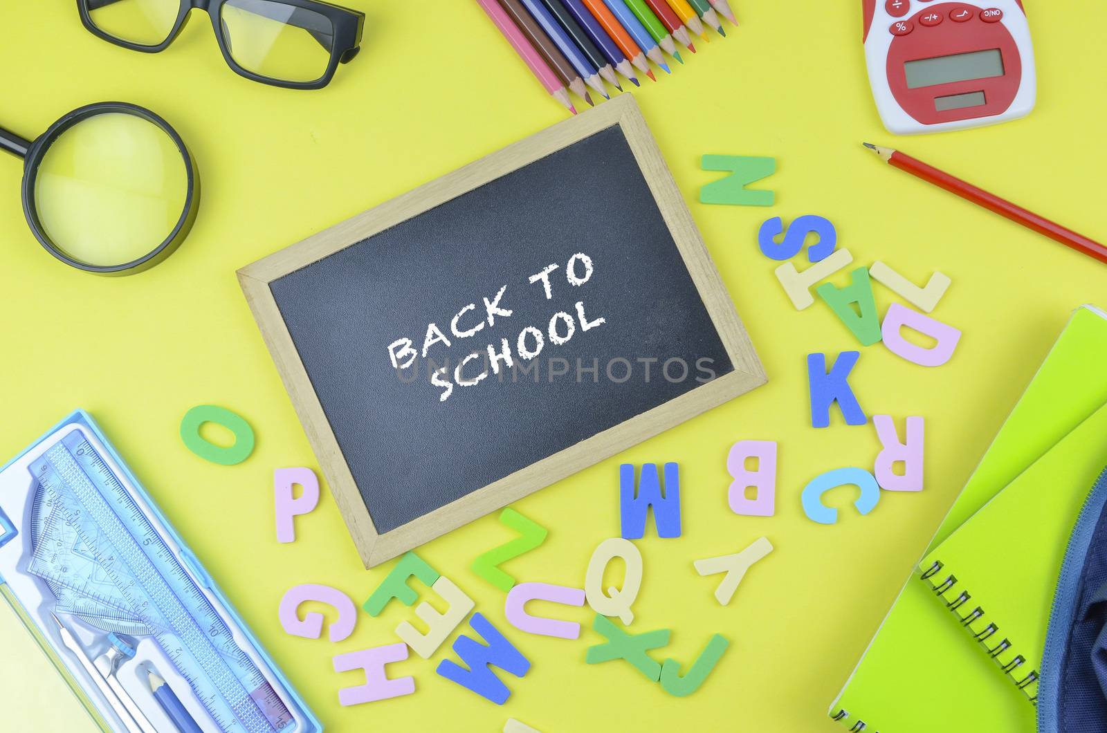 Student backpack and various school supplies. Studying, education and back to school concept. Yellow background and selective focus.