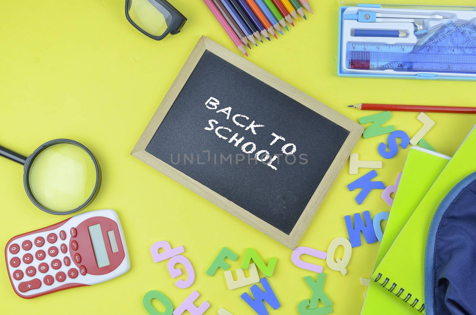 Student backpack and various school supplies. Studying, education and back to school concept. Yellow background and selective focus.