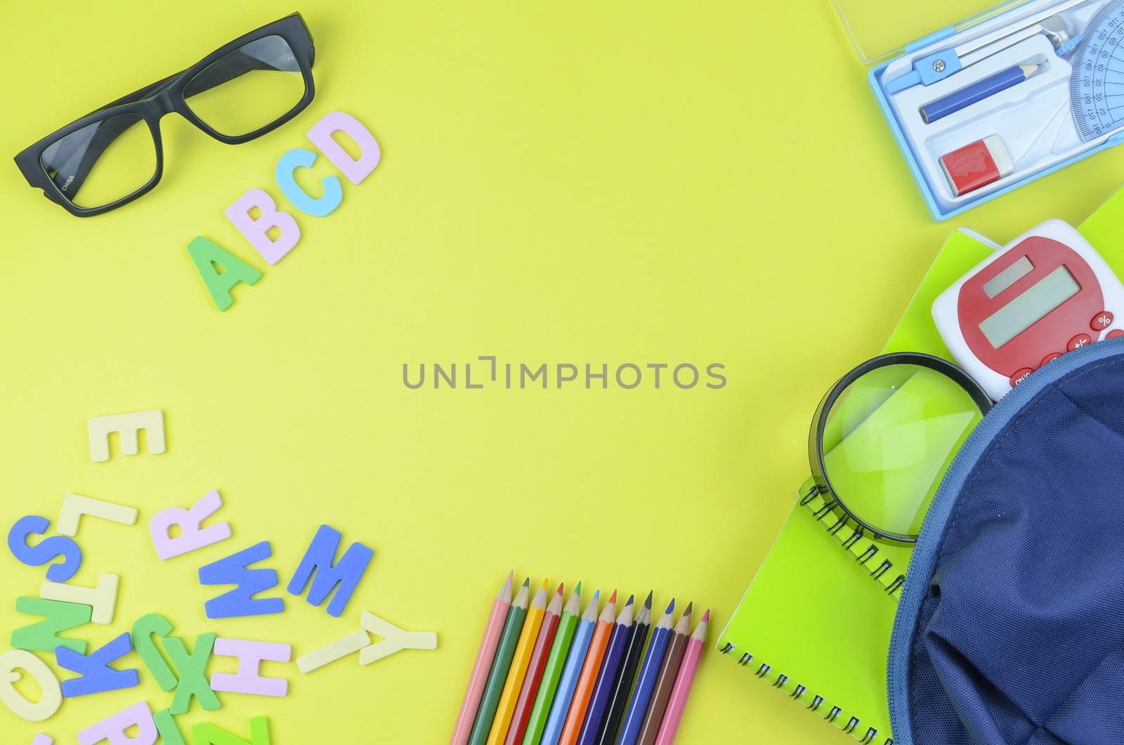 Student backpack and various school supplies. Studying, education and back to school concept. Yellow background and selective focus.