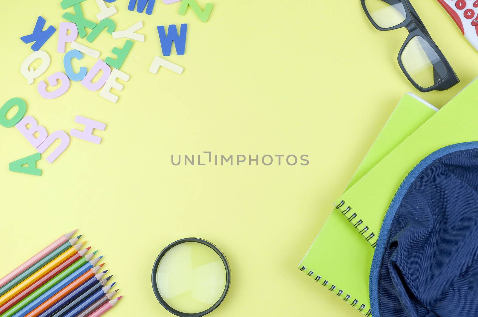 Student backpack and various school supplies. Studying, education and back to school concept. Yellow background and selective focus.