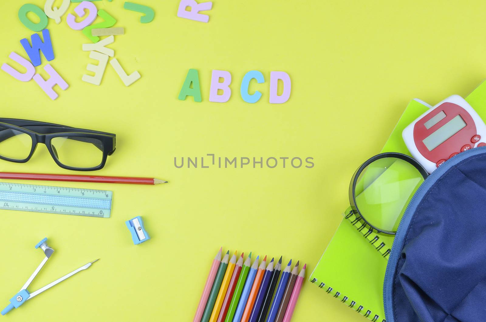 Student backpack and various school supplies. Studying, education and back to school concept. Yellow background and selective focus.