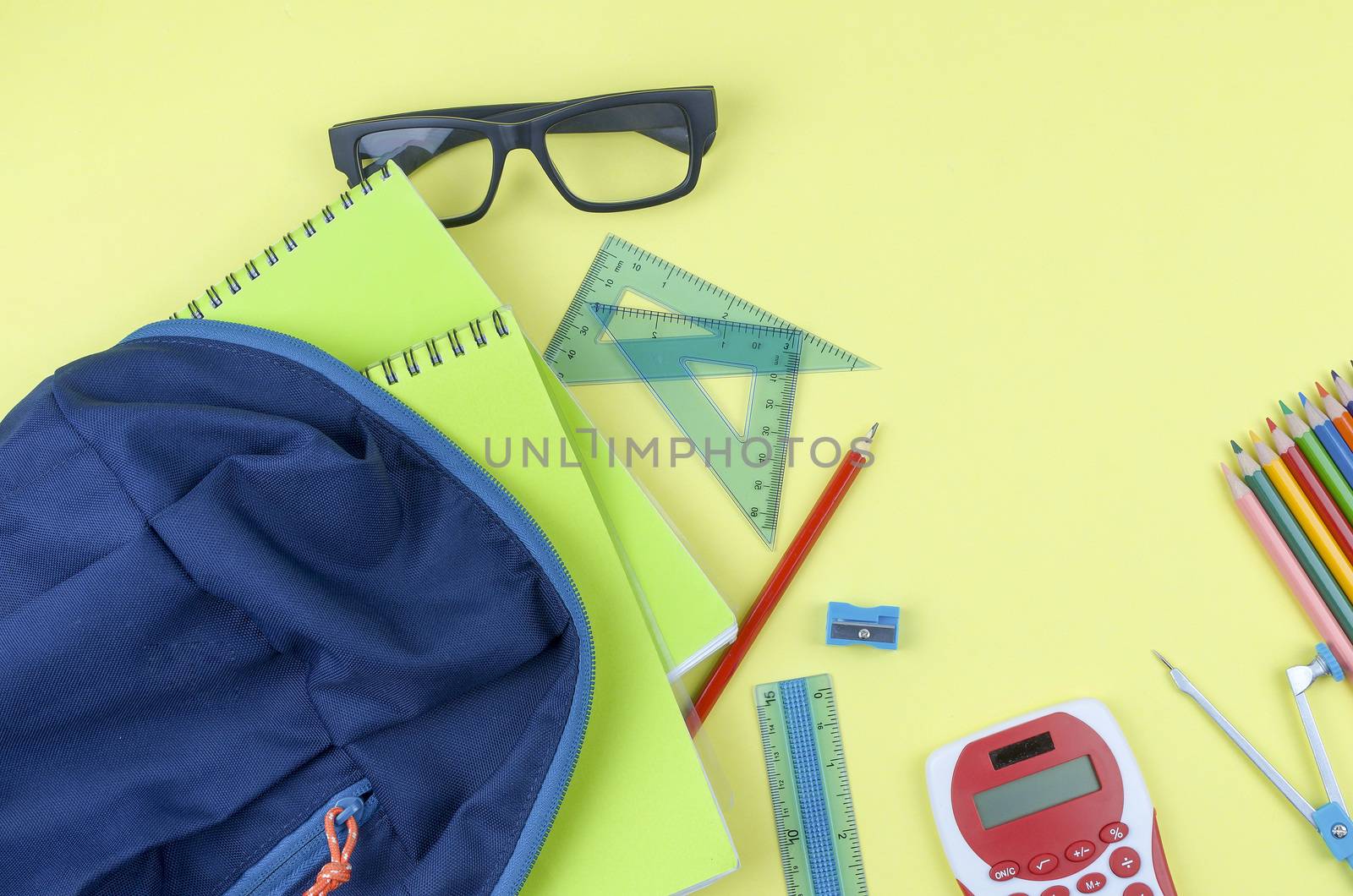 Student backpack and various school supplies. Studying, education and back to school concept. Yellow background and selective focus.