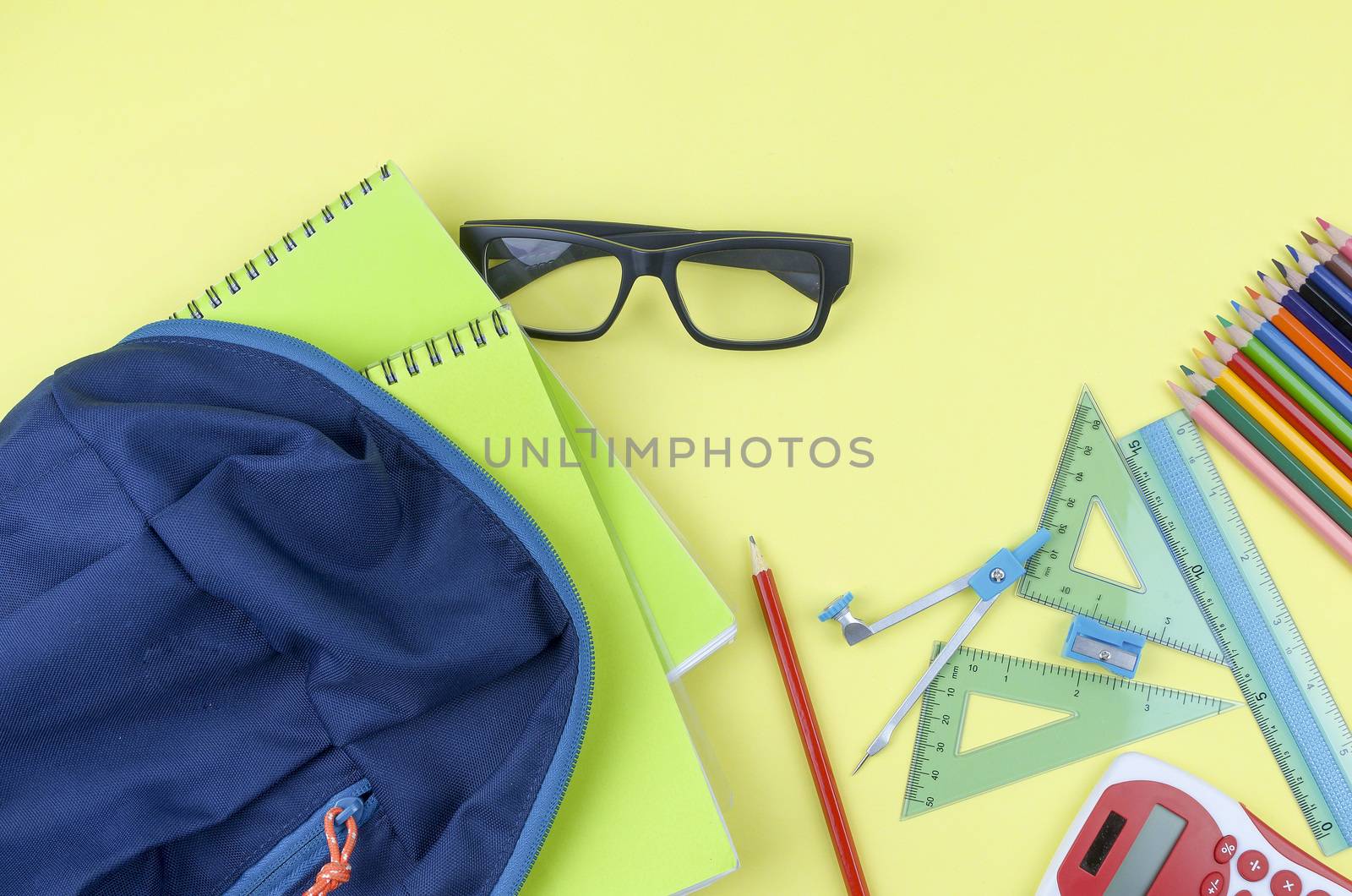 Student backpack and various school supplies. Studying, education and back to school concept. Yellow background and selective focus.