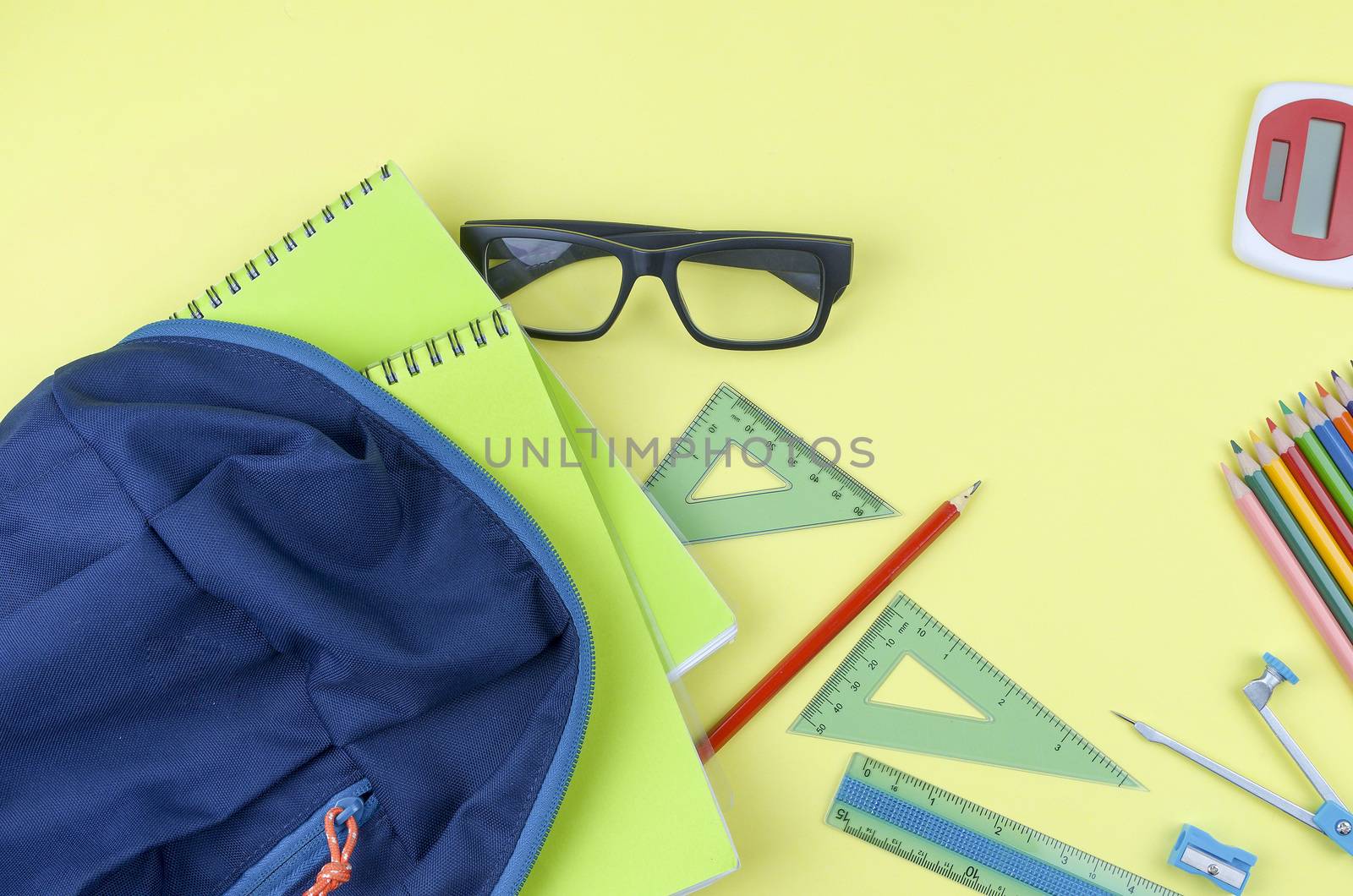 Student backpack and various school supplies. Studying, education and back to school concept. Yellow background and selective focus.