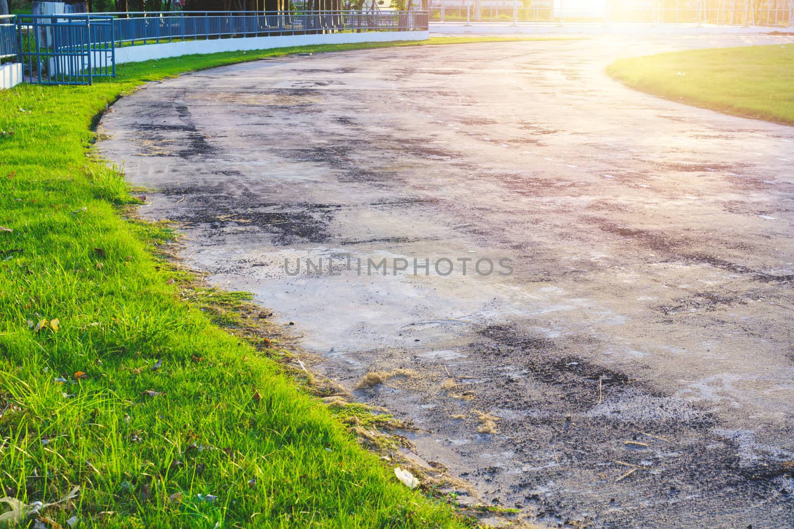 Old pathway and beautiful trees track for running or walking and cycling relax in the park on green grass field on the side of the Stadium. Sunlight and flare background concept.