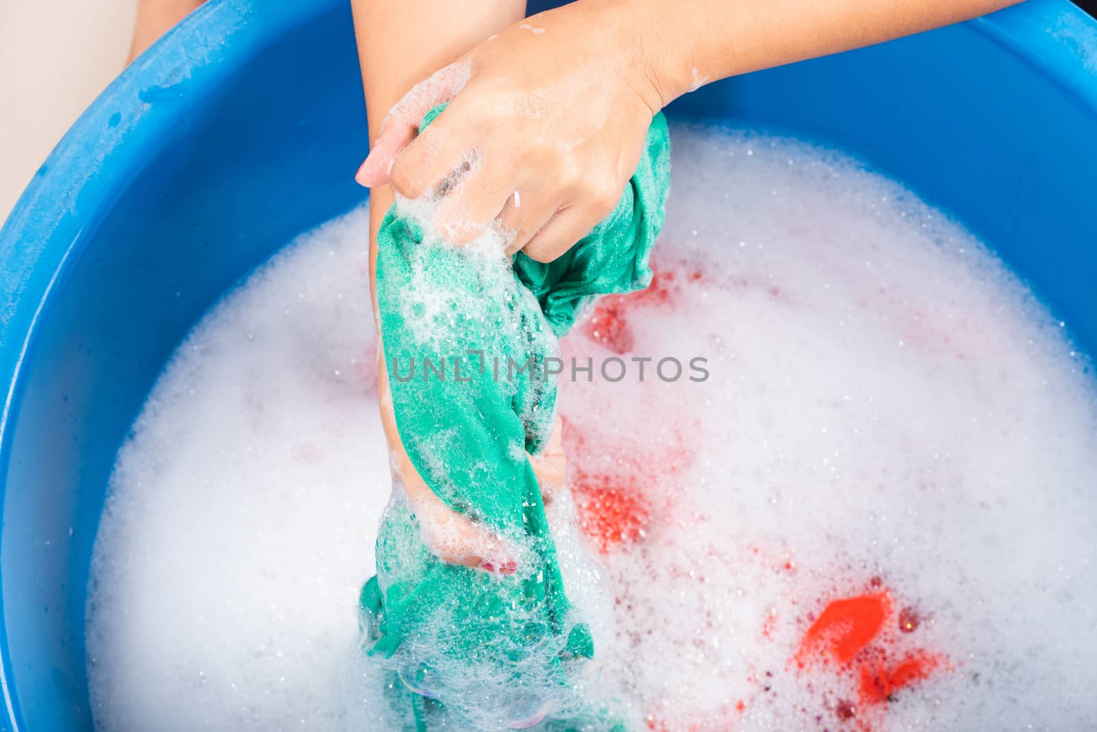 Closeup young Asian woman use hands washing color clothes in basin with detergent have soapy bubble water, studio shot background, laundry concept