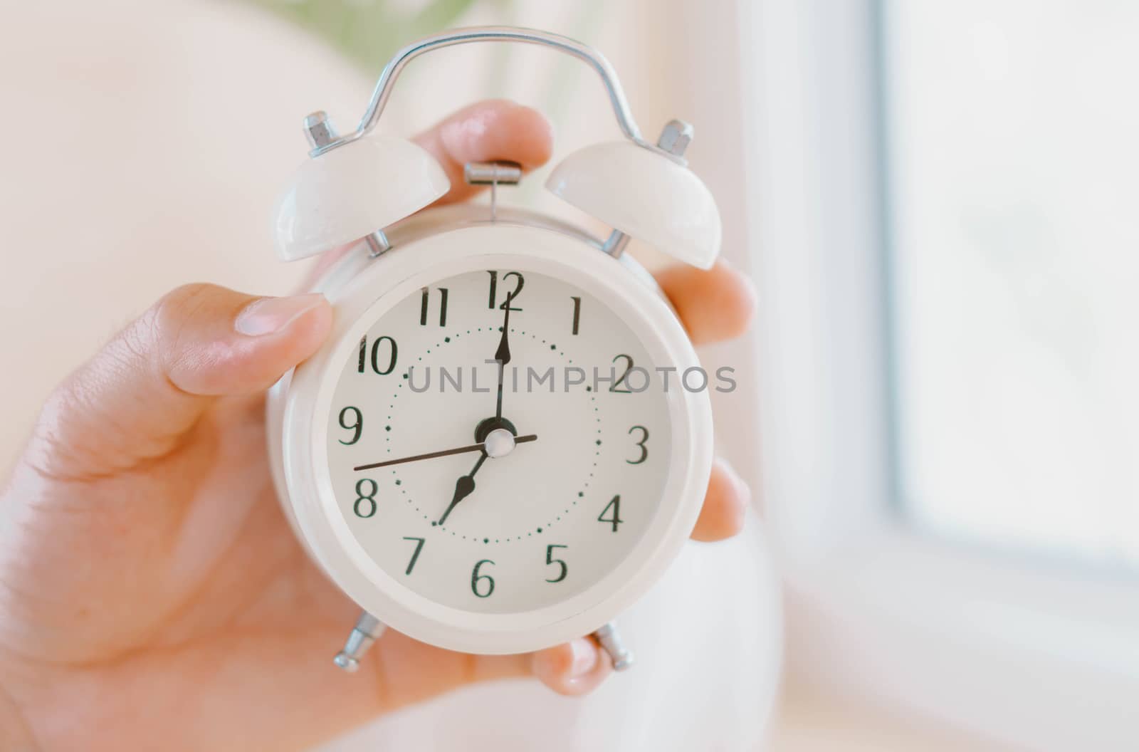 Closeup hand holding alarm clock on white table with soft light in the morning, selective