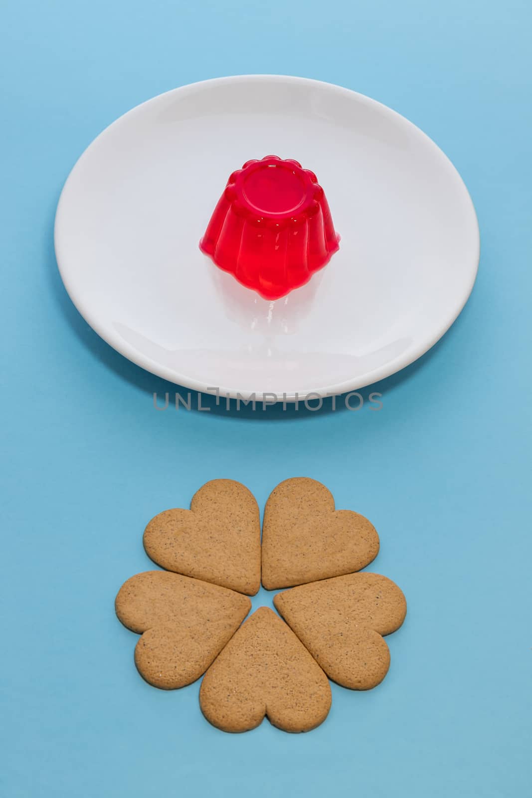 Close-up of a strawberry jelly dessert on a white plate. Heart-shaped cookies like a flower. Light blue background