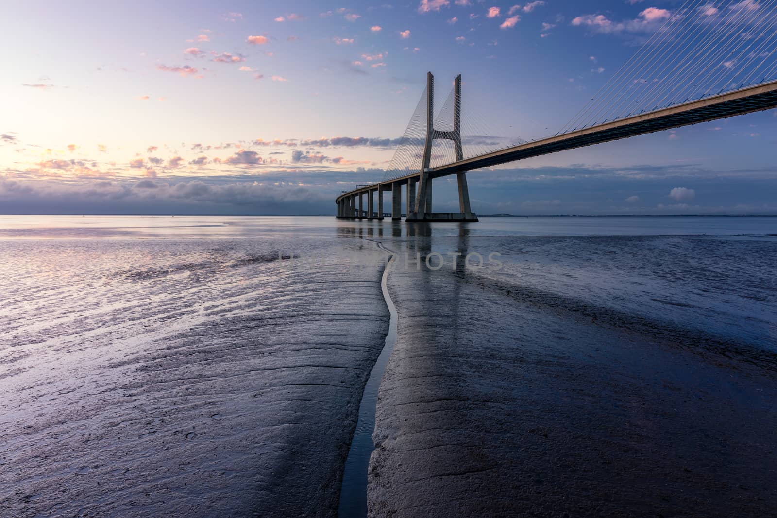 Vasco da Gama bridge at sunrise in Lisbon, Portugal. Vasco da Gama Bridge is a cable-stayed bridge flanked by viaducts and rangeviews that spans the Tagus River in Parque das Nações in Lisbon. 