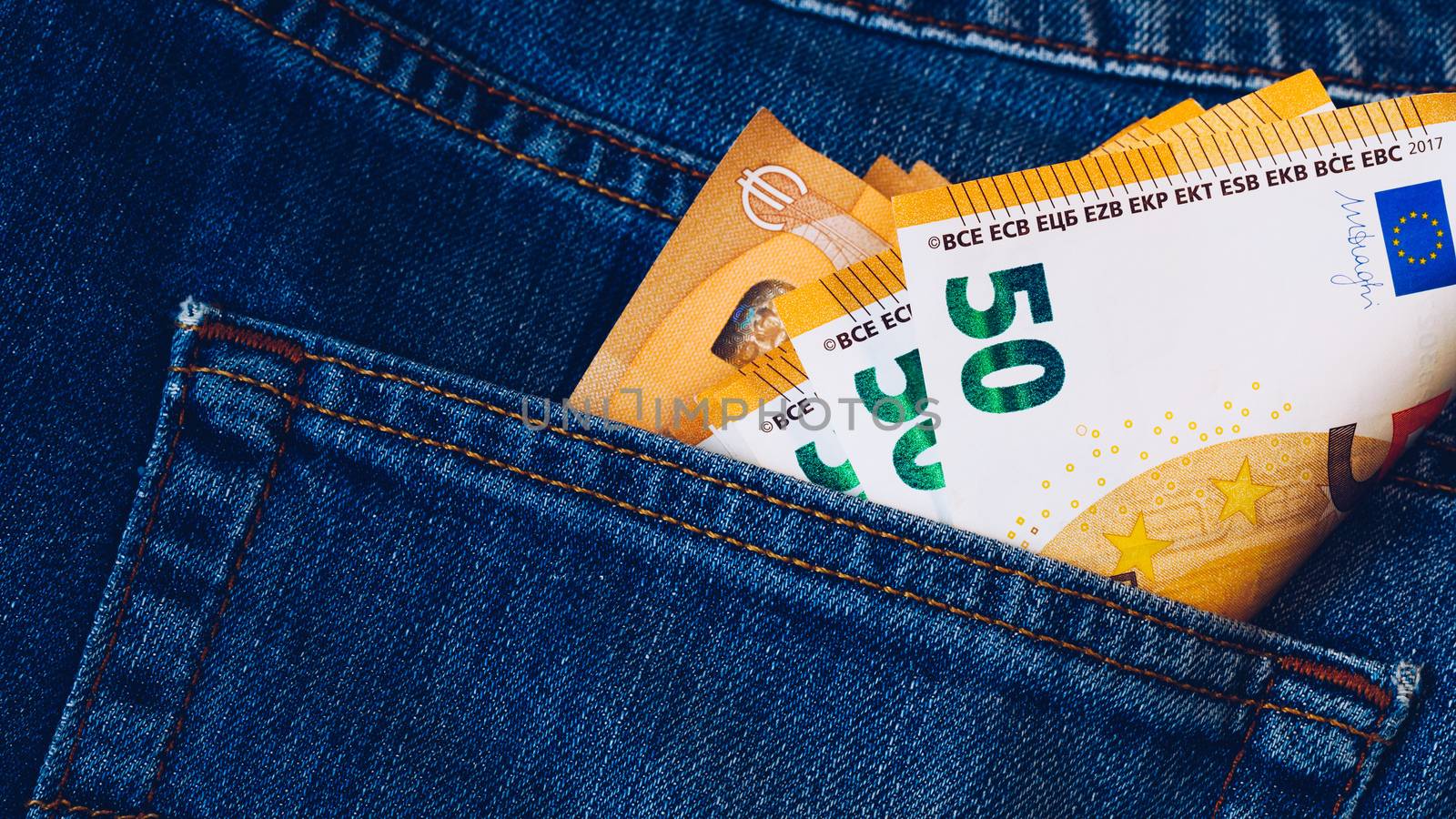 Euro bills in jeans pocket background. Euro banknotes in jeans back pocket. Concept of rich people, saving or spending money. Euro bills falling out. Easy to steal the money. Irresponsible action.