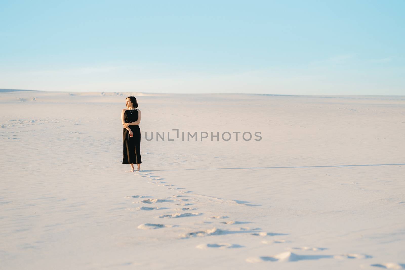 girl in a black dress stands in the middle of the desert against the background of footprints