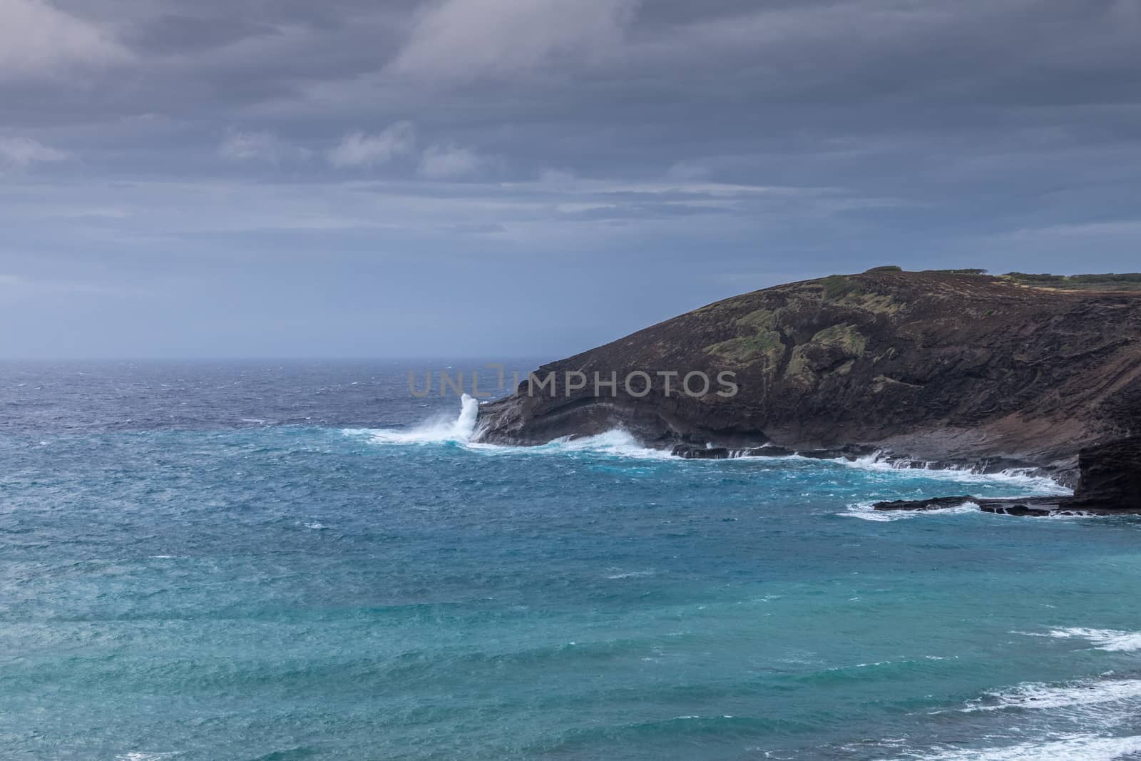 Oahu, Hawaii, USA. - January 11, 2020: Hanauma Bay Nature Preserve. White crashing waves of azure water on face of baboon cliff rock under heavy rain cloudscape.