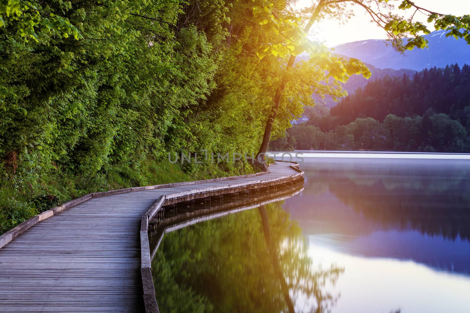 Wooden walkway around the lake Bled with mountains and houses on the background. Beautiful Slovenian Nature. Bled, Slovenia, Europe. 
