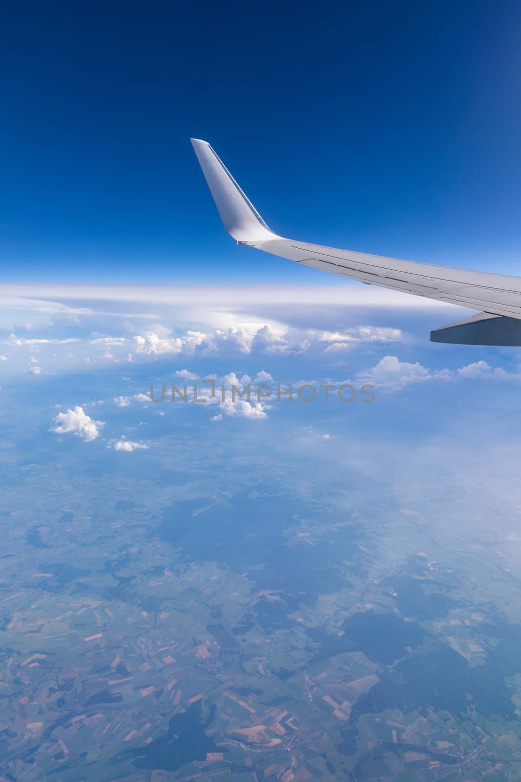 View of the wing of an airplane flying above the clouds at high altitude under a blue sky from the passenger window. In flight over Europe. View of jet airplane wing flying in blue sky over clouds.