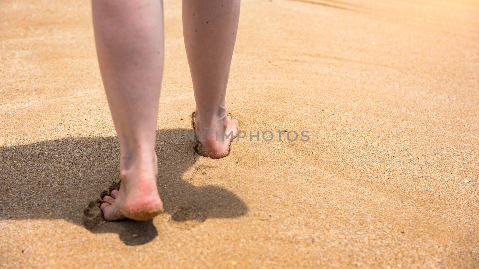 Woman walking barefoot on a beach. Close up leg of young woman walking along wave of sea water and sand on the summer beach. Travel Concept. Woman walking on sand beach leaving footprints in the sand.