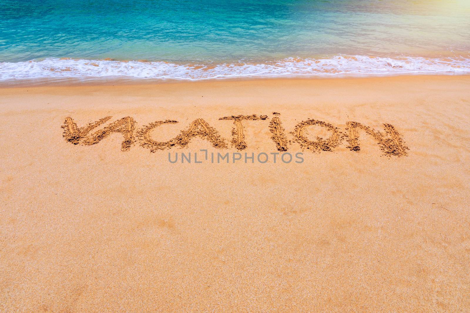 Vacation text on a beach. Vacation written in a sandy tropical beach. "Vacation" written in the sand on the beach blue waves in the background. Vacation on the sand beach concept.