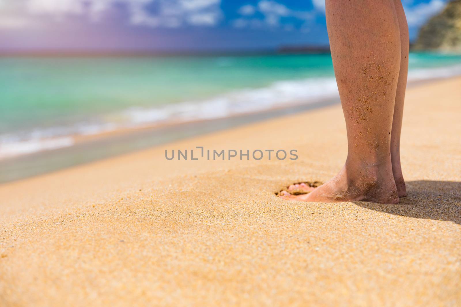 Closeup on leg of young woman standing on sea shore. Woman legs and feet walking on the sand of the beach with the sea water in the background. Woman standing on the beach with wave sea.