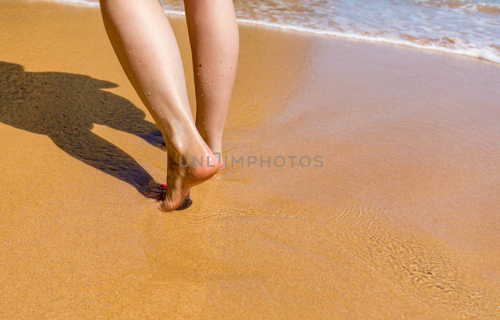 Woman walking barefoot on a beach. Close up leg of young woman walking along wave of sea water and sand on the summer beach. Travel Concept. Woman walking on sand beach leaving footprints in the sand.