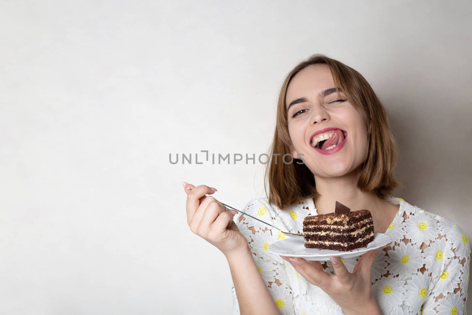 Happy grimacing woman eats tasty chocolate cake over a grey background. Empty space